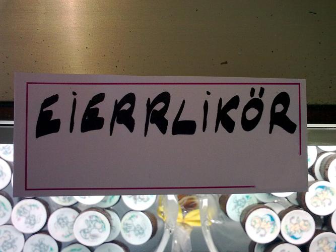 Ein Kärtchen, handgeschrieben, in einer Bäckerei, mit dem Wort: Eierrlikör (Eier mit Doppel-r)