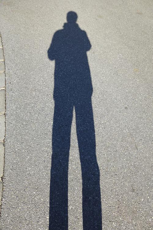 mein Schatten mit riesenlangen Beinen auf Asphalt